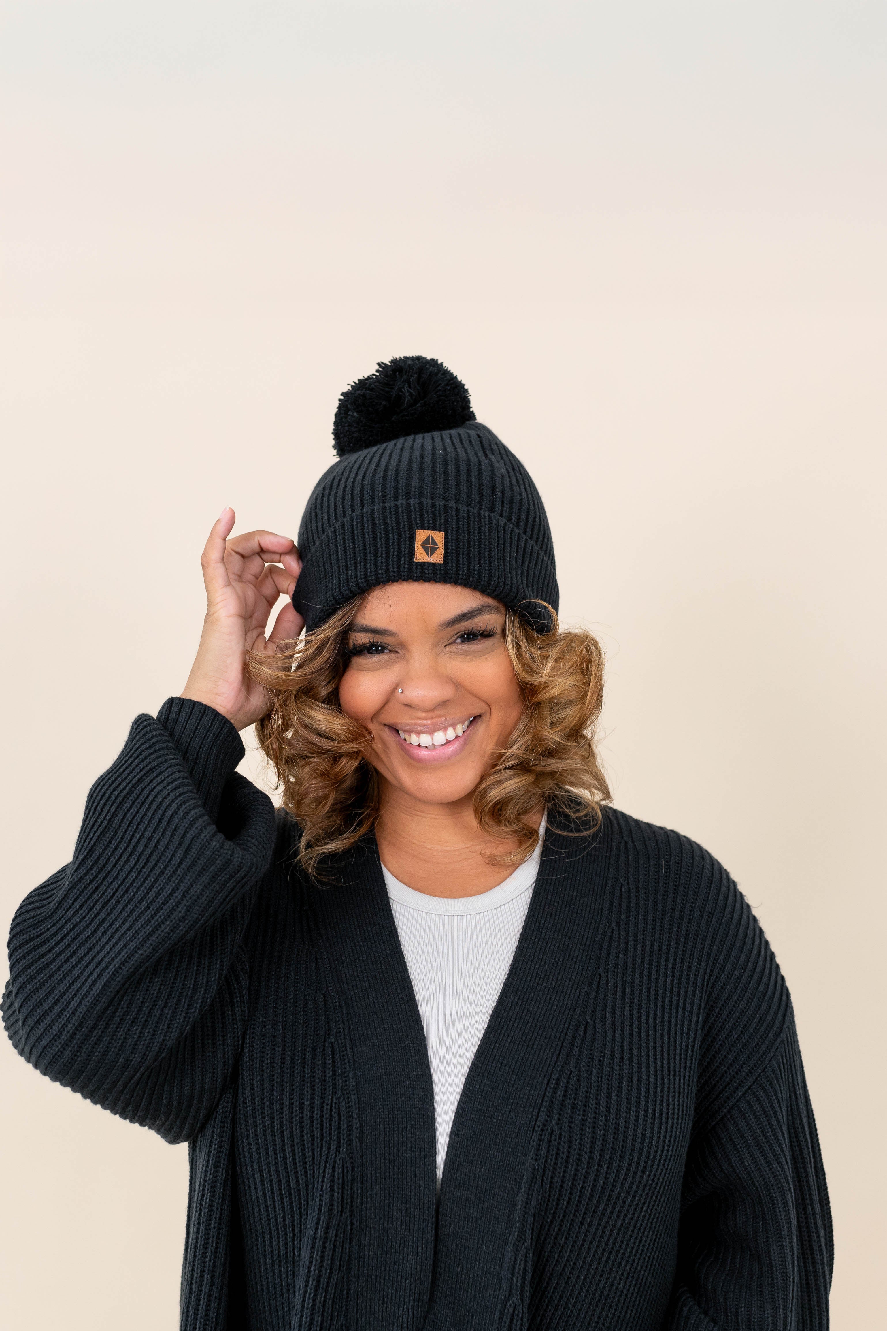 Model wearing  the Chunky Knit Adult Pom Beanie in Midnight with one hand on the brim of the beanie