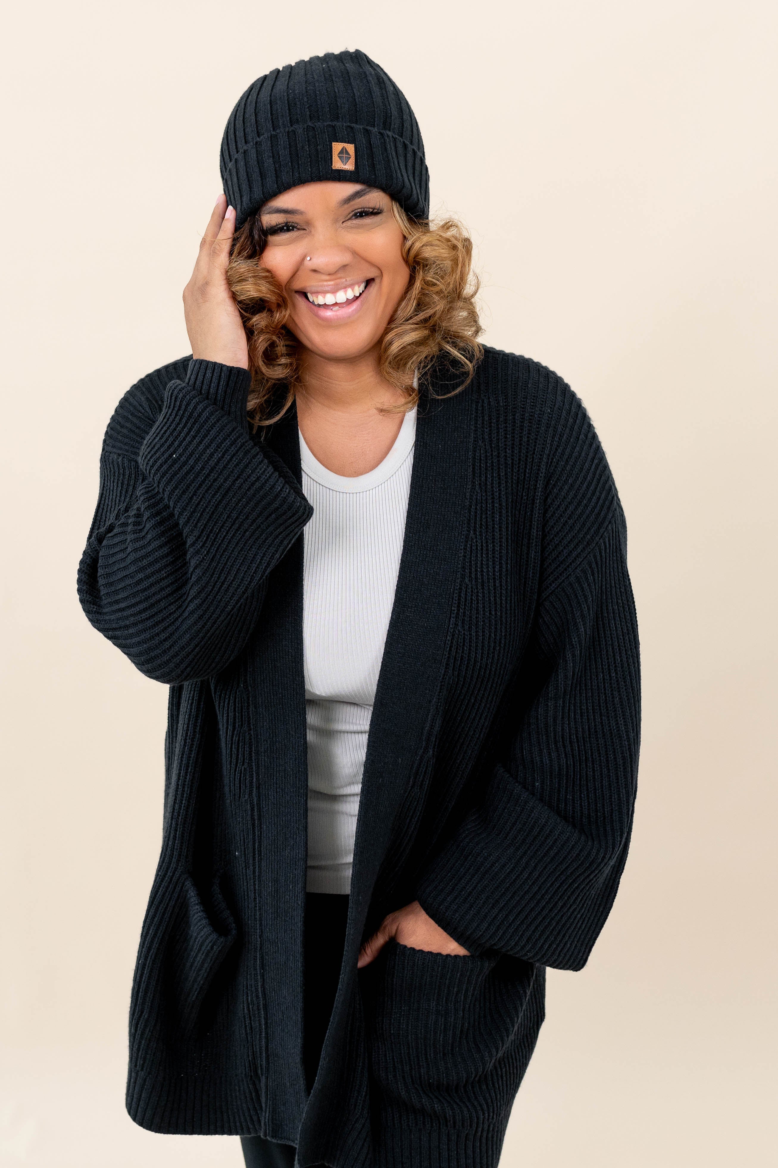 Smiling model wearing the Chunky Knit Adult Ribbed Beanie in Midnight with the Kyte Baby Leather logo visible