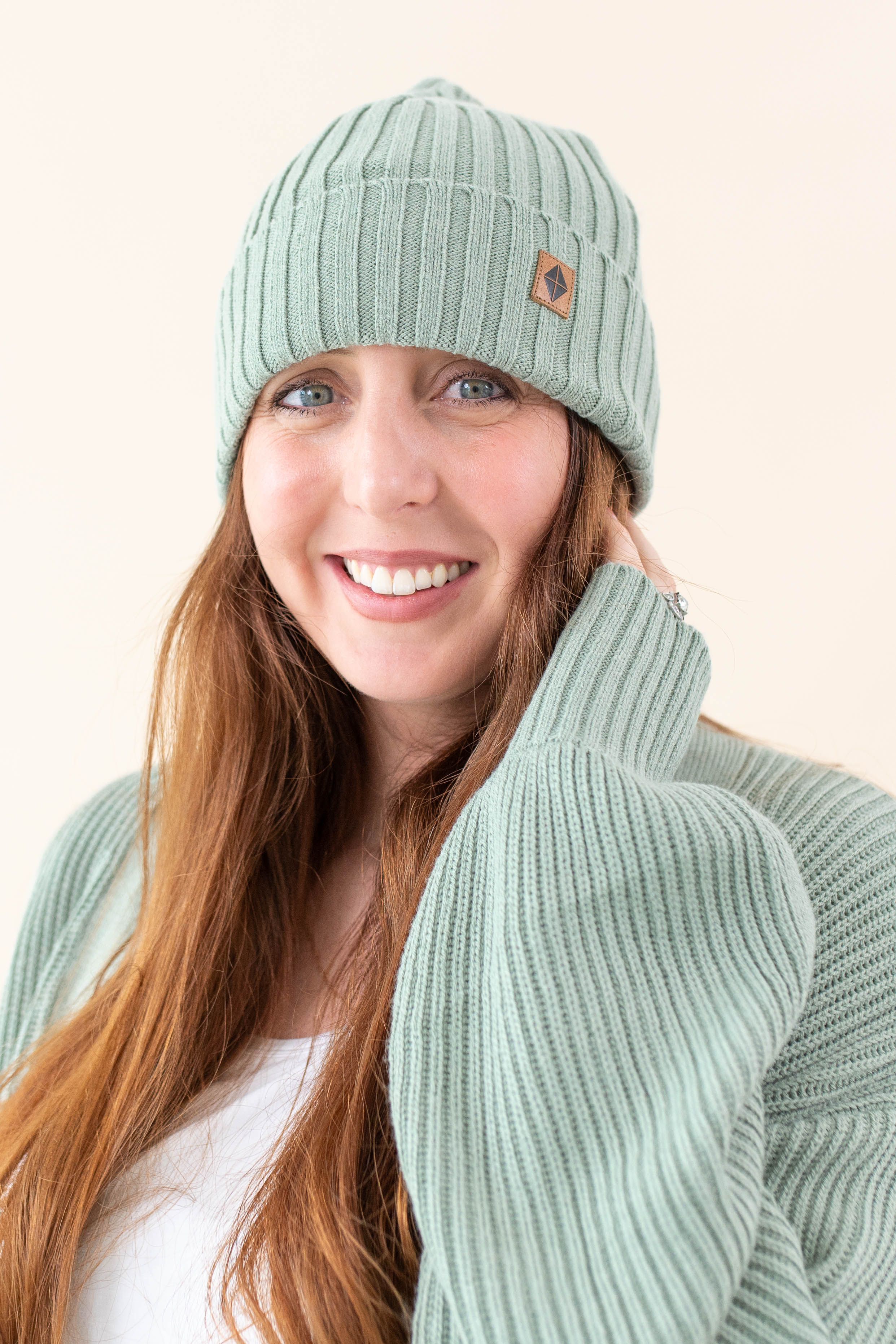 Smiling model wearing the Chunky Knit Adult Ribbed Beanie in Thyme with the Kyte Baby Leather logo visible