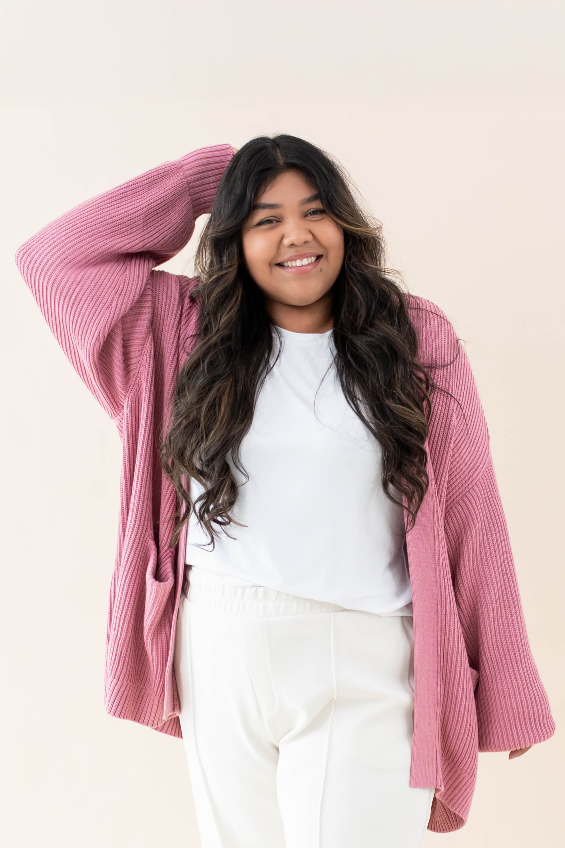 Model wearing the Chunky Knit Women's Oversized Cardigan in Apple Blossom with a white shirt and white pants