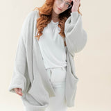 Female modeling the Chunky Knit Women's Oversized Cardigan in Oat paired with a white shirt and white pants