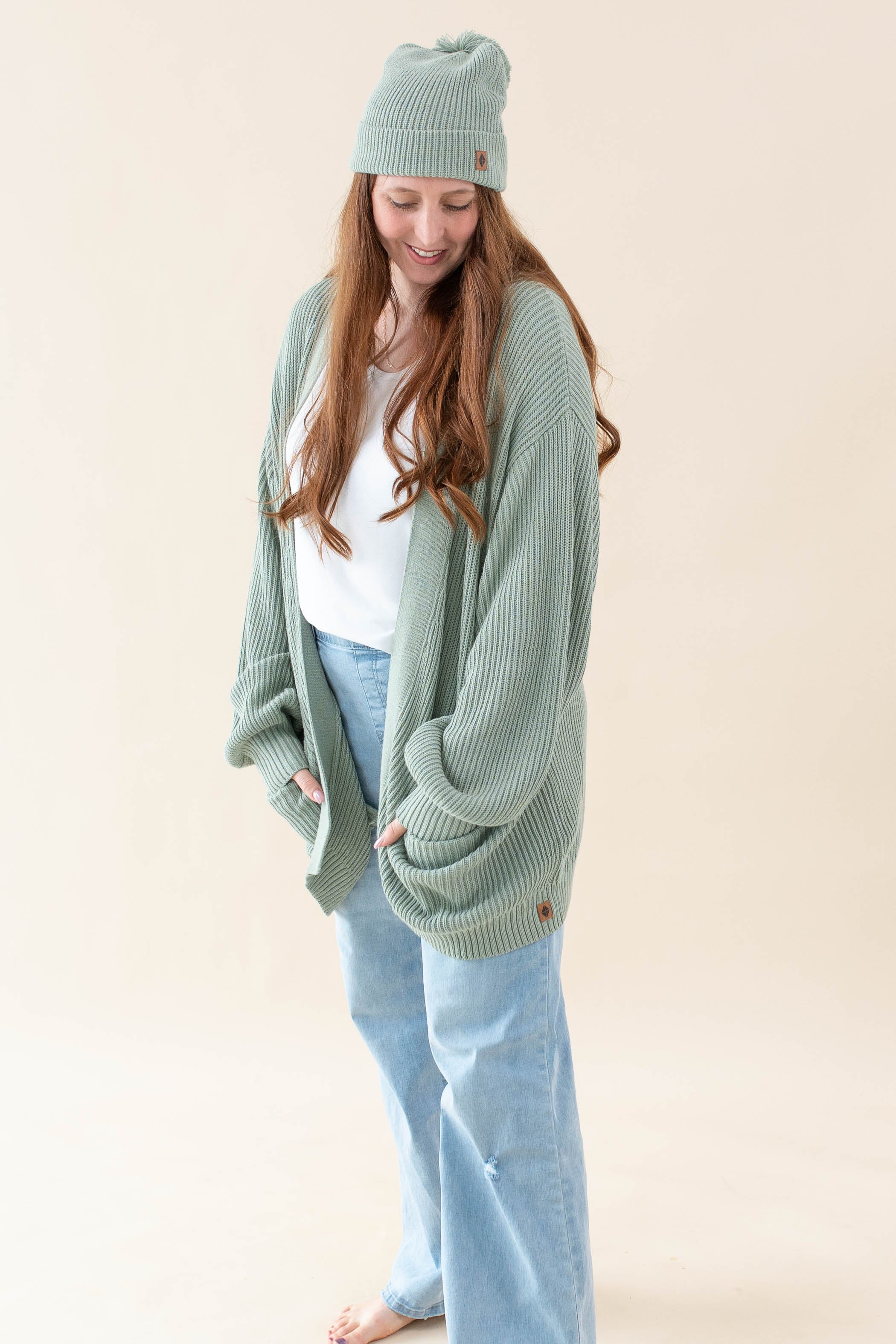 Model wearing the Chunky Knit Women's Oversized Cardigan in Thyme with a white shirt, light wash jeans and a Thyme Beanie