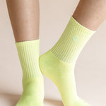 A close-up of a person's feet and lower legs wearing bright neon yellow-green crew socks against a solid pale beige background.