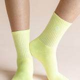 A close-up of a person's feet and lower legs wearing bright neon yellow-green crew socks against a solid pale beige background.
