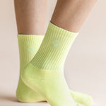 A close-up of a person's feet wearing light neon yellow crew socks against a soft beige background.