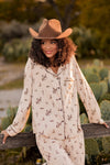 Female model leaning up against a wooden fence post wearing the Long-Sleeved Women's Pajama Set in Classic Cowboy with a brown cowboy hat   ::: Model is 5'8" wearing size S ///