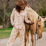 Female model wearing the Long-Sleeved Women's Pajama Set in Classic Cowboy and cowboy hat standing beside a real horse