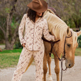 Female model wearing the Long-Sleeved Women's Pajama Set in Classic Cowboy and cowboy hat standing beside a real horse