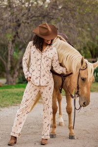 Female model wearing the Long-Sleeved Women's Pajama Set in Classic Cowboy and cowboy hat standing beside a real horse