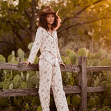 Female model wearing the Long-Sleeved Women's Pajama Set in Classic Cowboy leaning against a fence outside in front of cacti and trees   ::: Model is 5'8" wearing size S ///
