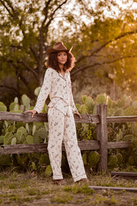 Female model wearing the Long-Sleeved Women's Pajama Set in Classic Cowboy leaning against a fence outside in front of cacti and trees   ::: Model is 5'8" wearing size S ///