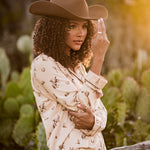 Female model wearing the Long-Sleeved Women's Pajama Set in Classic Cowboy and cowboy hat leaning up against a fence