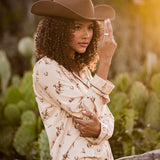 Female model wearing the Long-Sleeved Women's Pajama Set in Classic Cowboy and cowboy hat leaning up against a fence