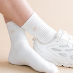 White socks with a subtle pattern worn with white sneakers on a beige background