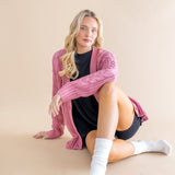 Woman wearing a pink cardigan over a black dress on a beige background