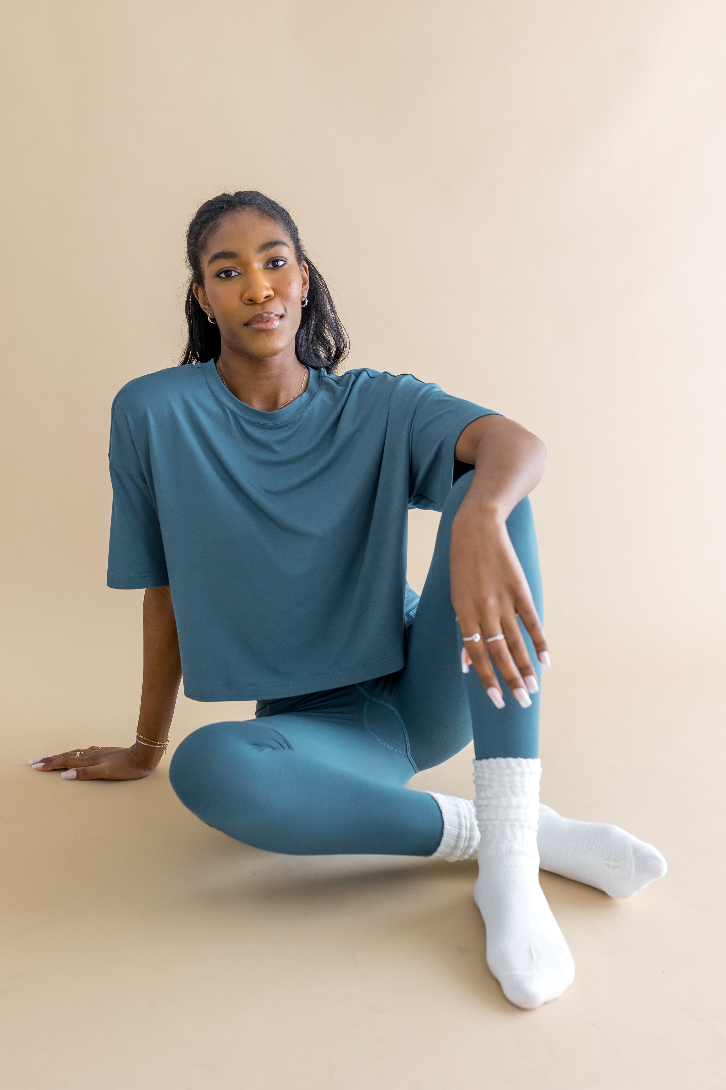 Woman wearing a blue outfit and white scrunch socks sitting on a beige background