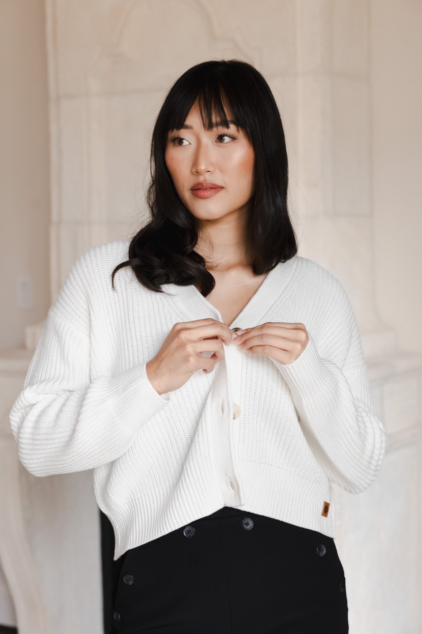 Woman looking to the side buttoning her cropped cardigan in cloud
