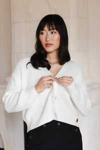 Woman looking to the side buttoning her cropped cardigan in cloud