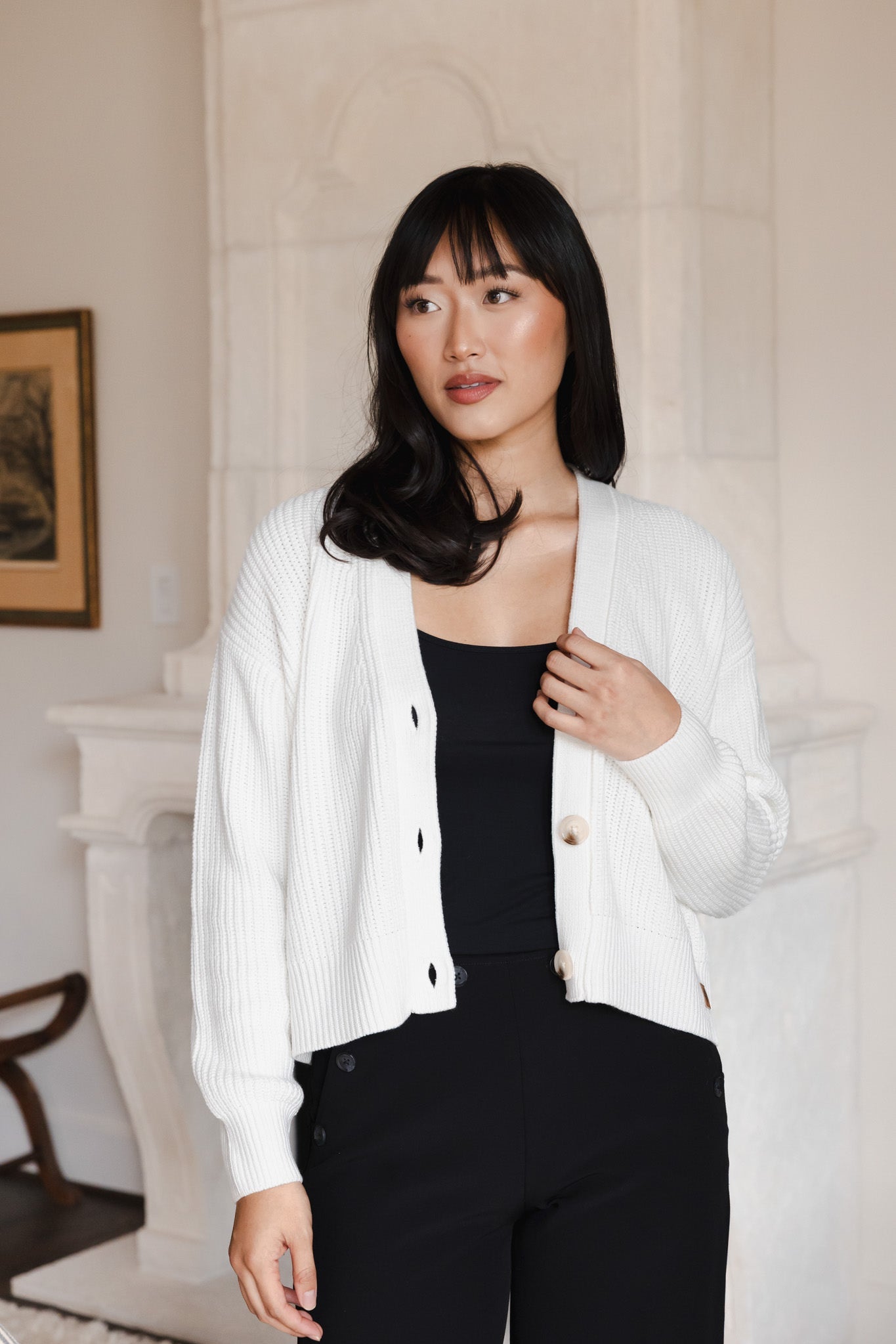 Modal posing in Chunky Knit Women's Cropped Cardigan in Cloud over black camisole and pants standing in a living room