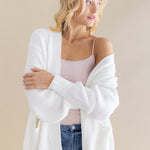 Female model posing wearing the Chunky Knit Women's Oversized Cardigan in Cloud with a light pink camisole and light wash jeans