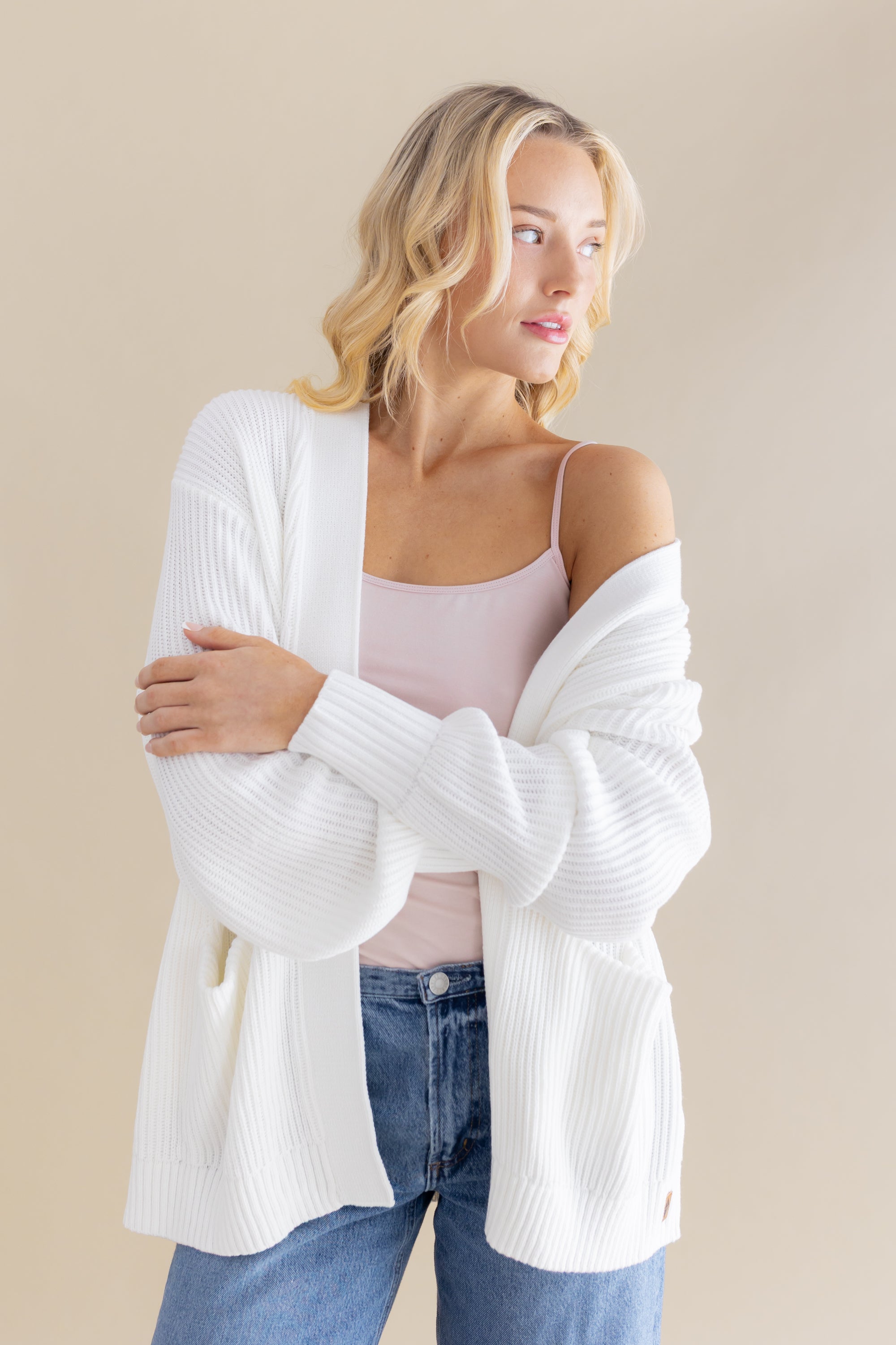 Female model posing wearing the Chunky Knit Women's Oversized Cardigan in Cloud with a light pink camisole and light wash jeans
