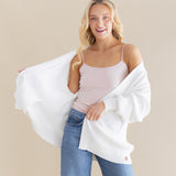 Female model posing wearing the Chunky Knit Women's Oversized Cardigan in Cloud around her shoulders paired with a light pink camisole and light wash jeans
