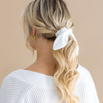 Woman with blonde hair styled in a ponytail with a white scrunchie on a beige background