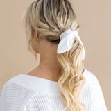 Woman with blonde hair styled in a ponytail with a white scrunchie on a beige background