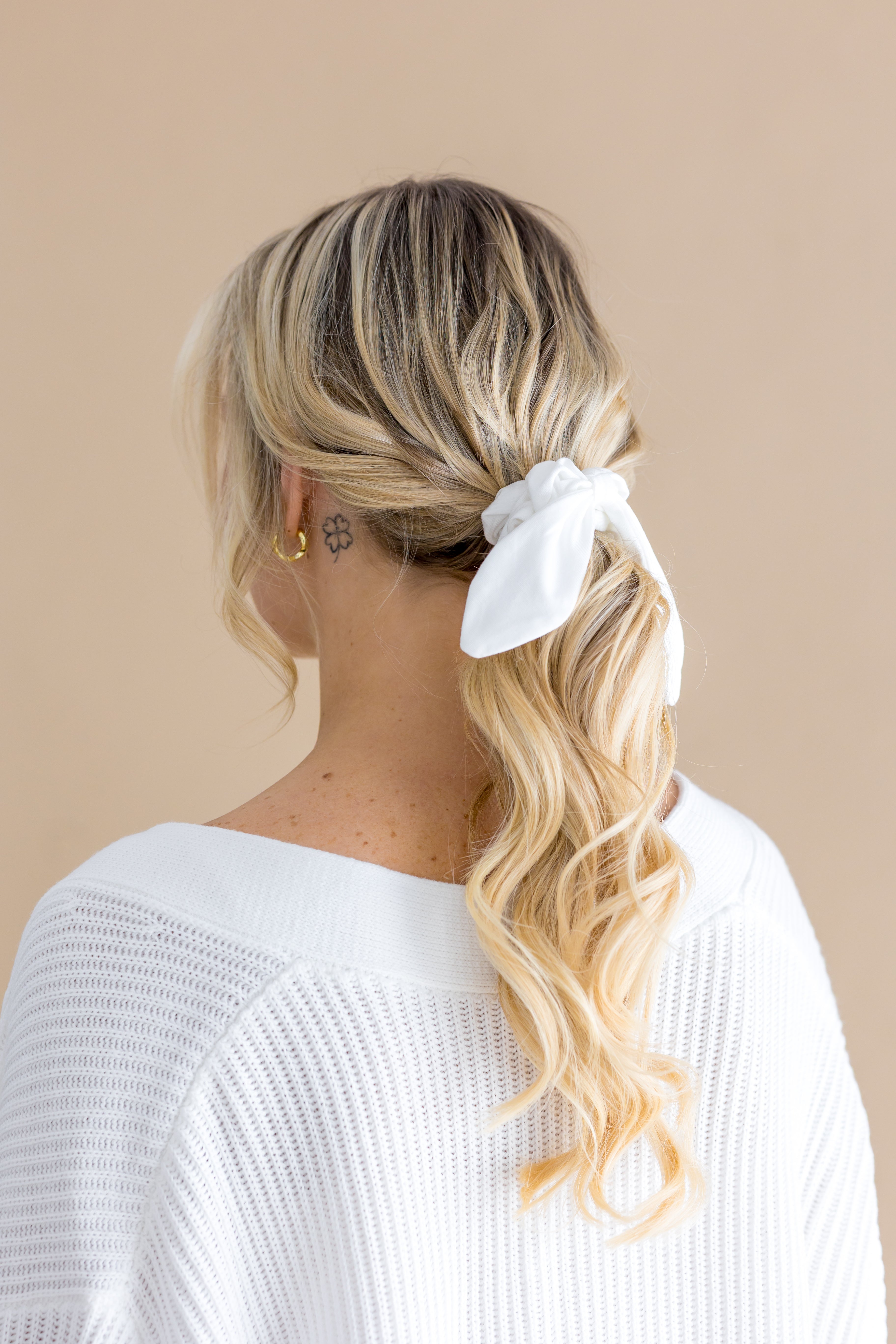 Woman with blonde hair styled in a ponytail with a white scrunchie on a beige background