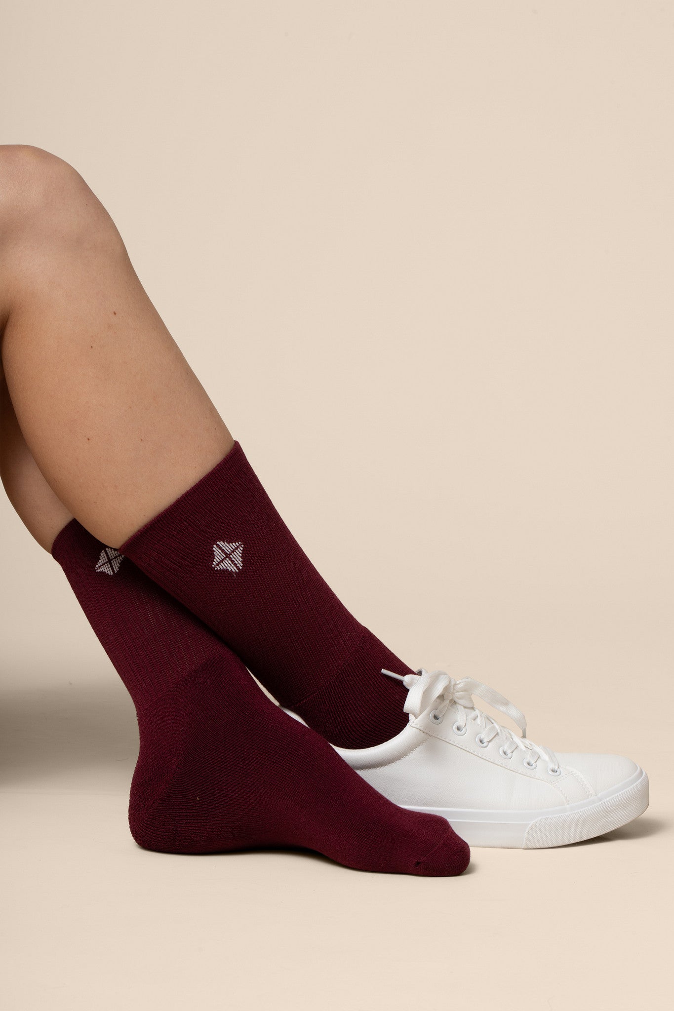 Burgundy socks with a logo worn by a person with a white sneaker on a beige background