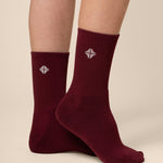 Burgundy socks with a logo worn by a person on a beige background