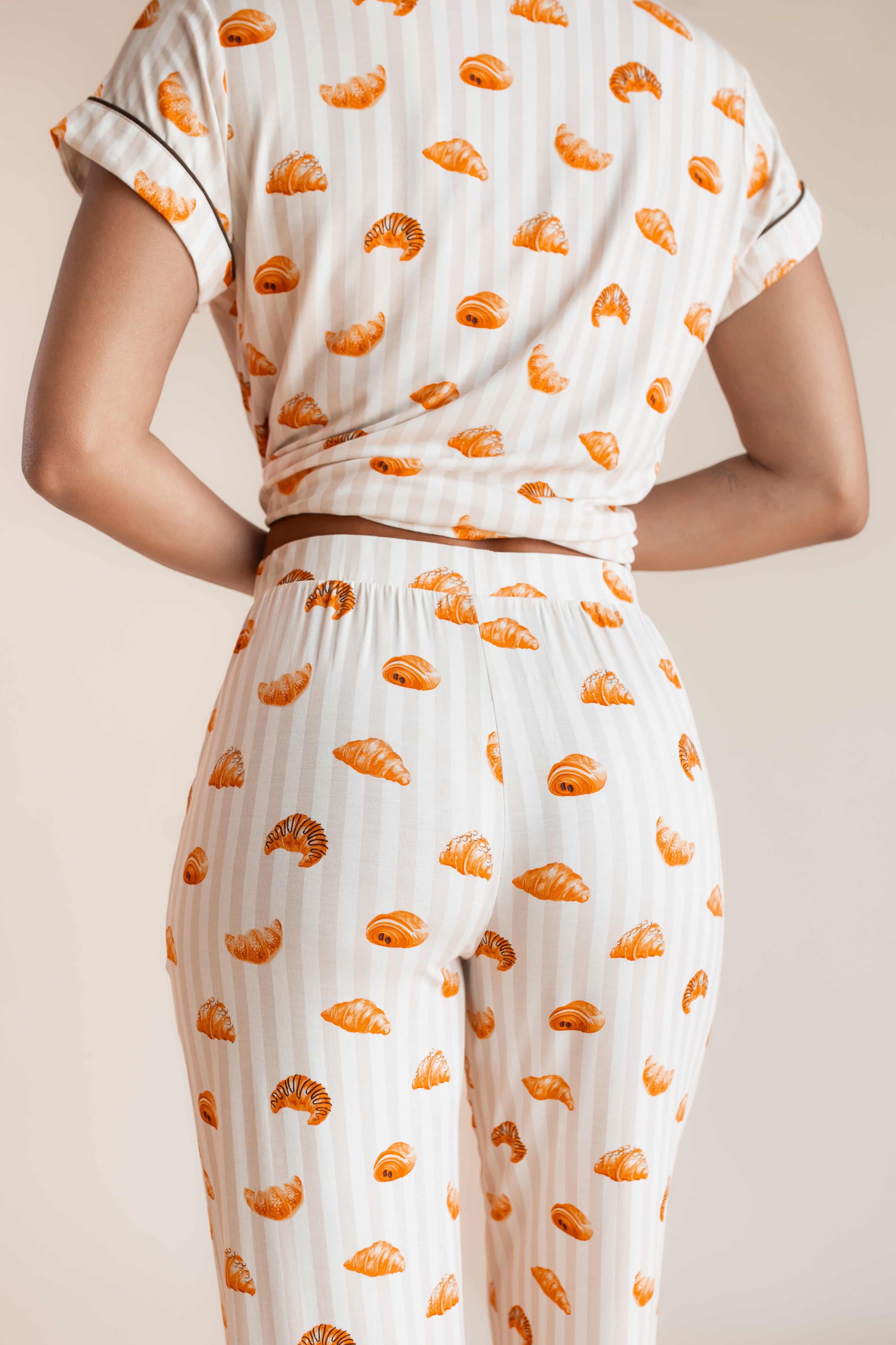 Model showcasing the backside of Women's Short Sleeve Cropped Pajama Set in Croissant print on a beige background