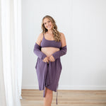 Woman wearing Scoop Neck Bralette in Currant and lounge robe standing in a room with white walls and wooden floor.