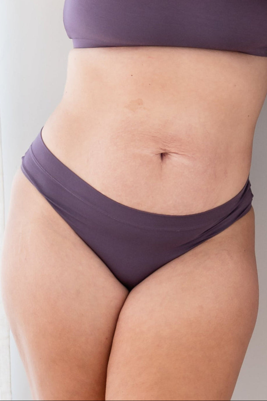 Woman in cheekini underwear and matching bralette in a deep purple color