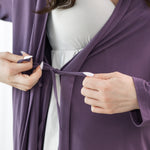 Person wearing a purple robe over a white dress, adjusting the robe.