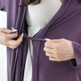 Person wearing a purple robe over a white dress, adjusting the robe.
