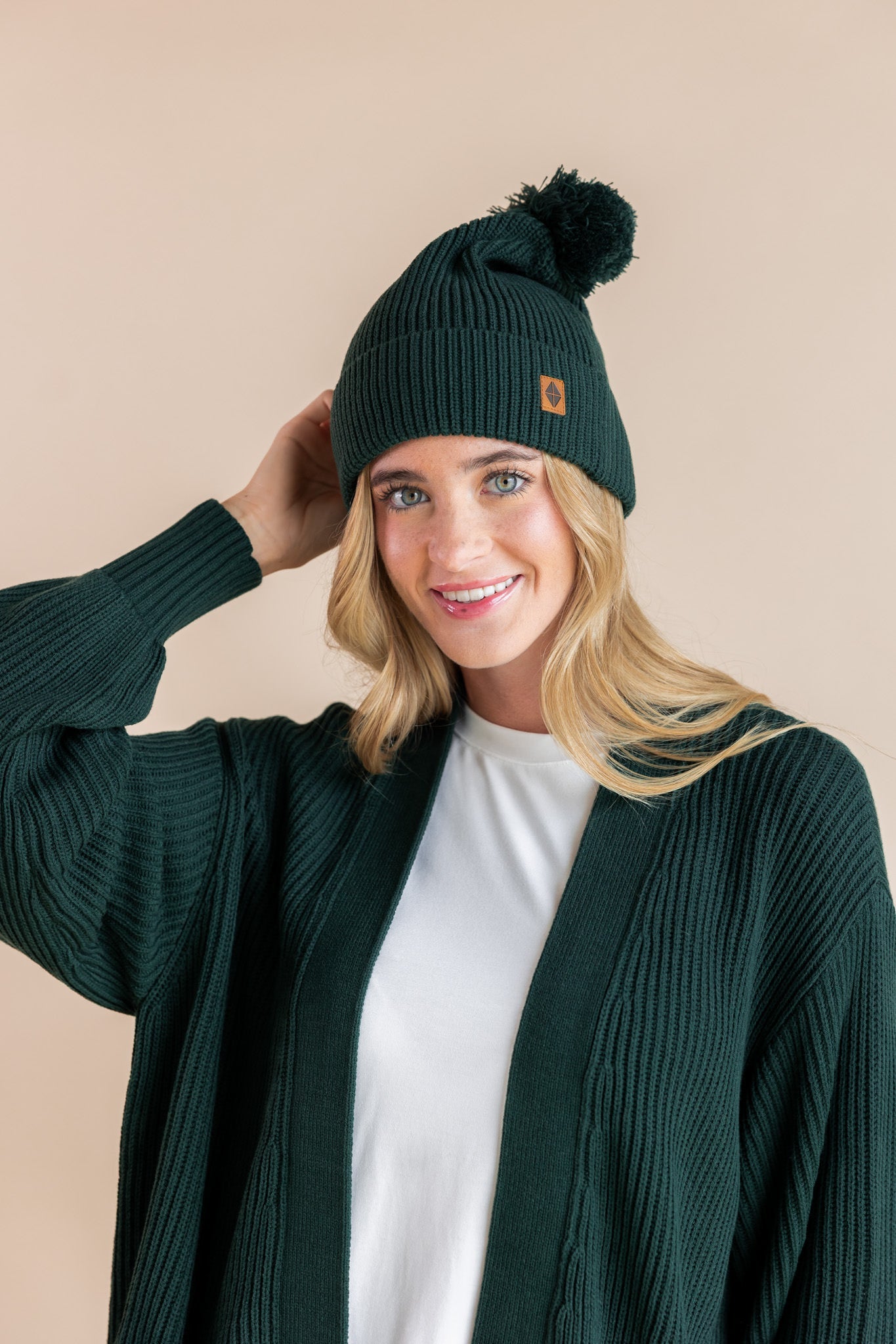 Modal wearing chunky knit Adult pom beanie in cypress and chunky knit oversized cardigan in cypress over white t-shirt on a beige background