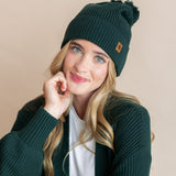 Modal wearing chunky knit Adult pom beanie in cypress and chunky knit oversized cardigan in cypress over white t-shirt on a beige background