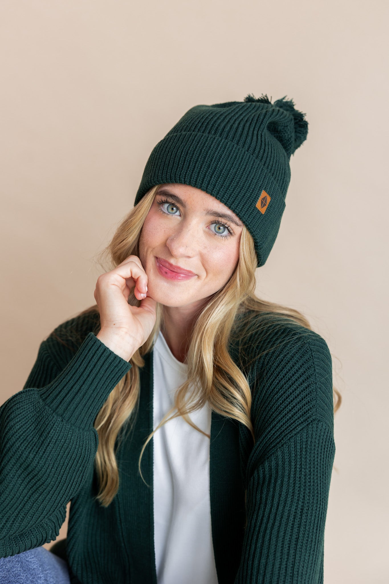 Modal wearing chunky knit Adult pom beanie in cypress and chunky knit oversized cardigan in cypress over white t-shirt on a beige background