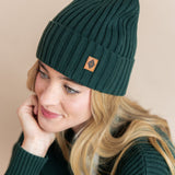 Modal wearing chunky knit Adult ribbed beanie in cypress and chunky knit oversized cardigan in cypress on a beige background