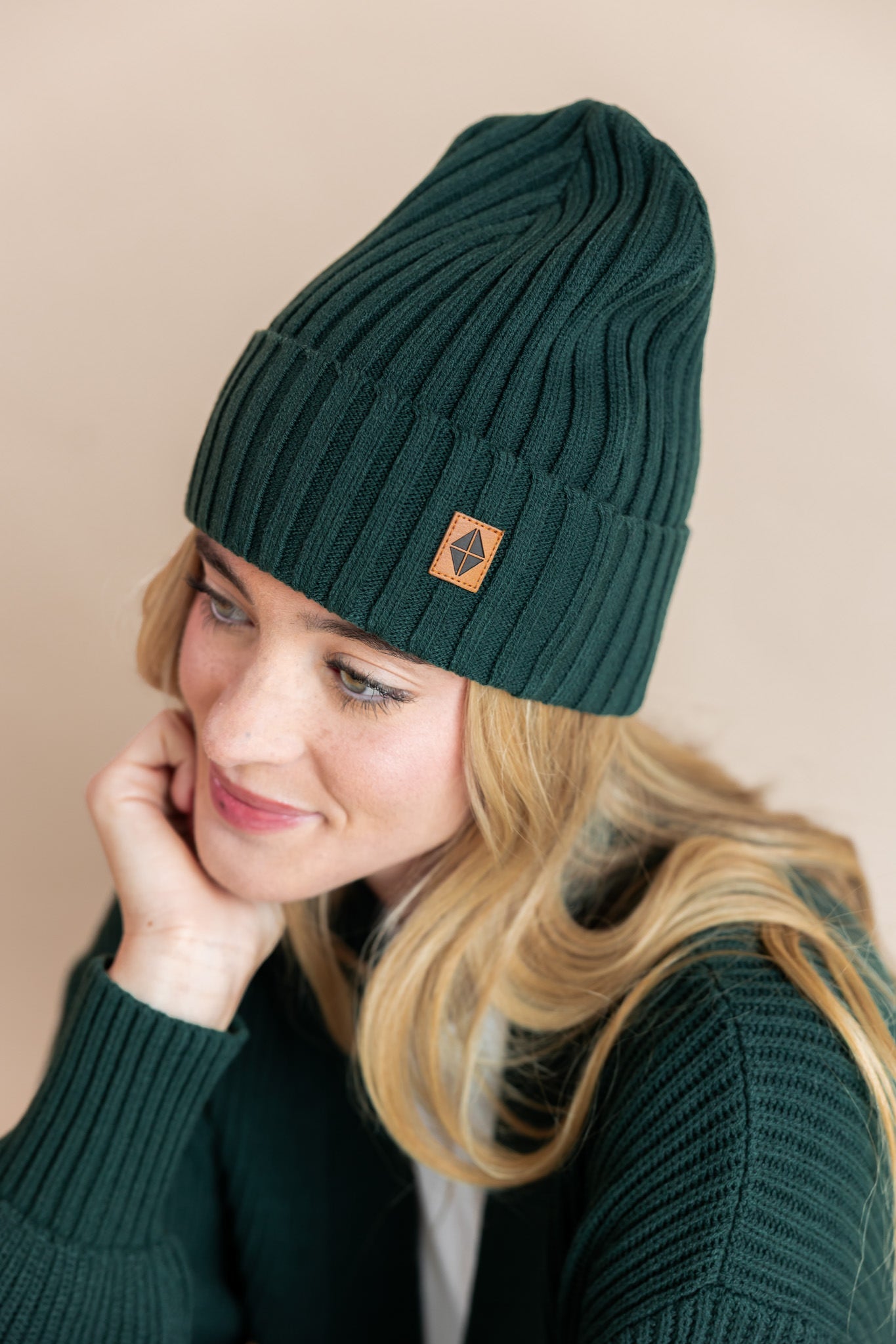 Modal wearing chunky knit Adult ribbed beanie in cypress and chunky knit oversized cardigan in cypress on a beige background