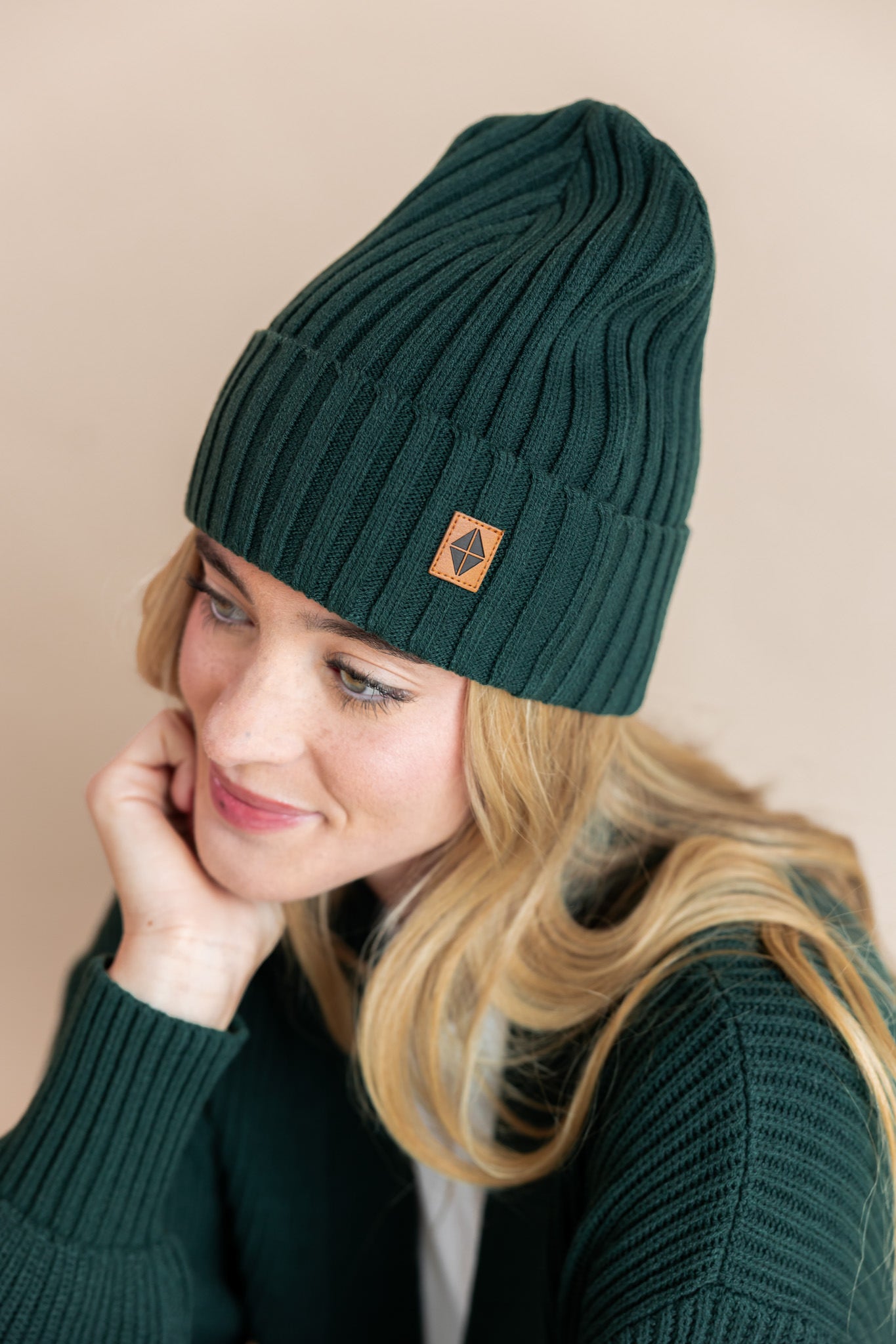 Modal wearing chunky knit Adult ribbed beanie in cypress and chunky knit oversized cardigan in cypress on a beige background