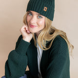 Modal wearing chunky knit Adult ribbed beanie in cypress over chunky knit oversized cardigan in cypress on a beige background