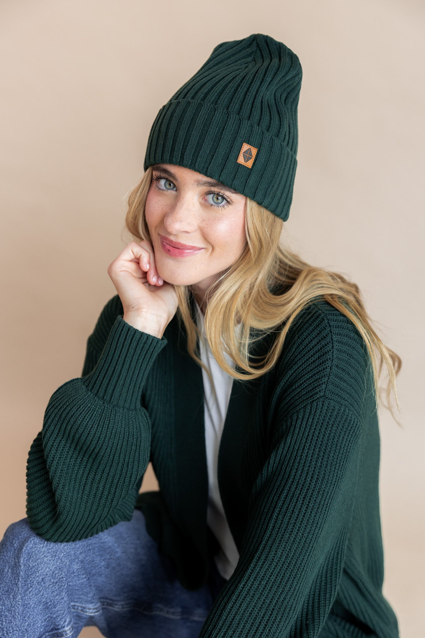 Modal wearing chunky knit Adult ribbed beanie in cypress over chunky knit oversized cardigan in cypress on a beige background