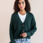 Modal posing in Chunky Knit Cropped Cardigan in cypress over white t-shirt and blue jeans on a beige background