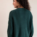 Modal showcasing back side of Chunky Knit Cropped Cardigan in cypress over blue jeans on a beige background