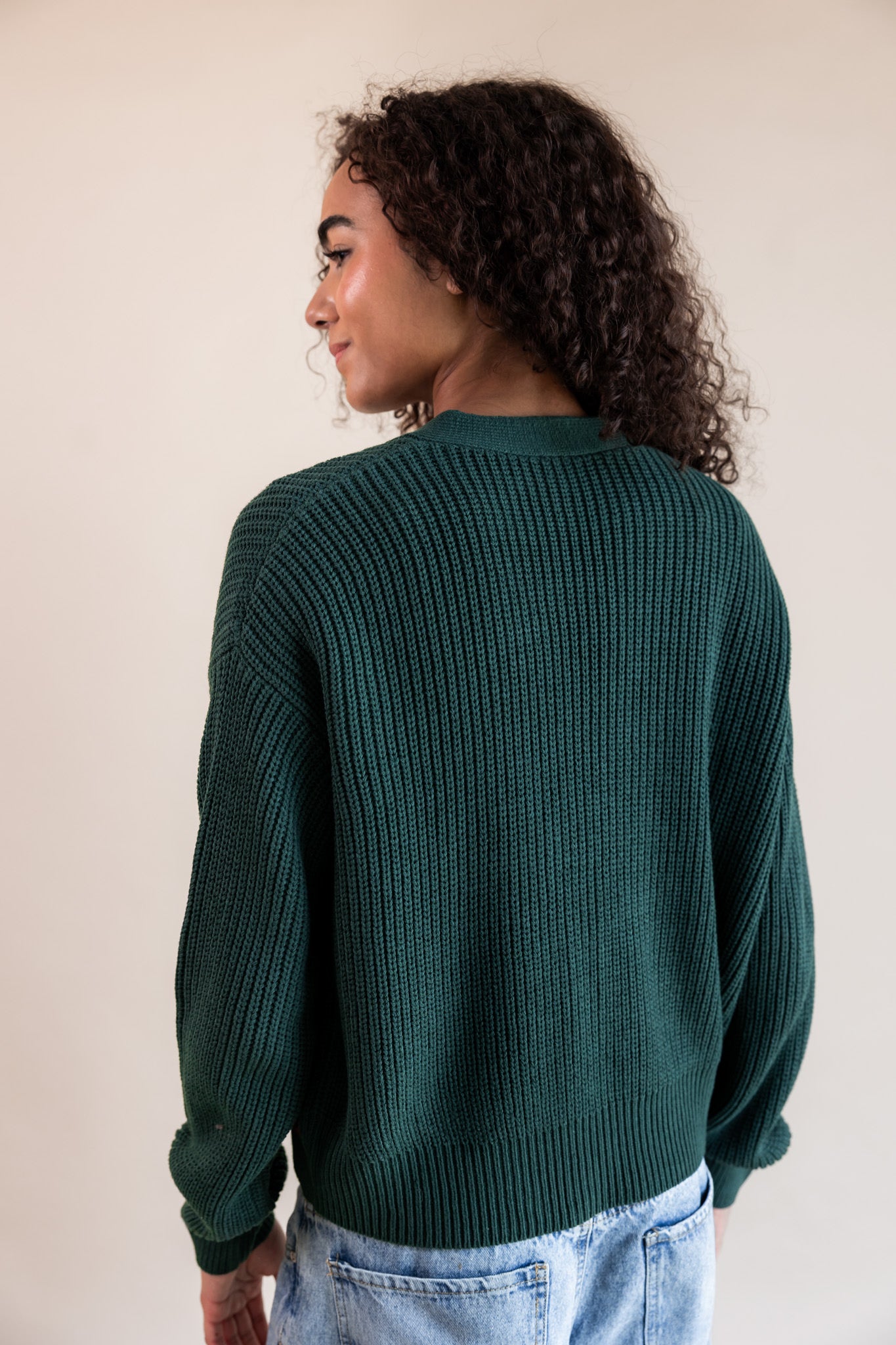 Modal showcasing back side of Chunky Knit Cropped Cardigan in cypress over blue jeans on a beige background