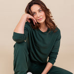 Woman sitting with one leg bent in and the other propped up resting her head on her hand looking up wearing a sweat shirt and sweatpants in cypress
::: Model is 5'10" wearing size M ///