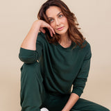 Woman sitting with one leg bent in and the other propped up resting her head on her hand looking up wearing a sweat shirt and sweatpants in cypress
::: Model is 5'10" wearing size M ///