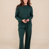 Woman wearing Women's Sweatpants in Cypress color under similar color women's sweatshirt on a beige background